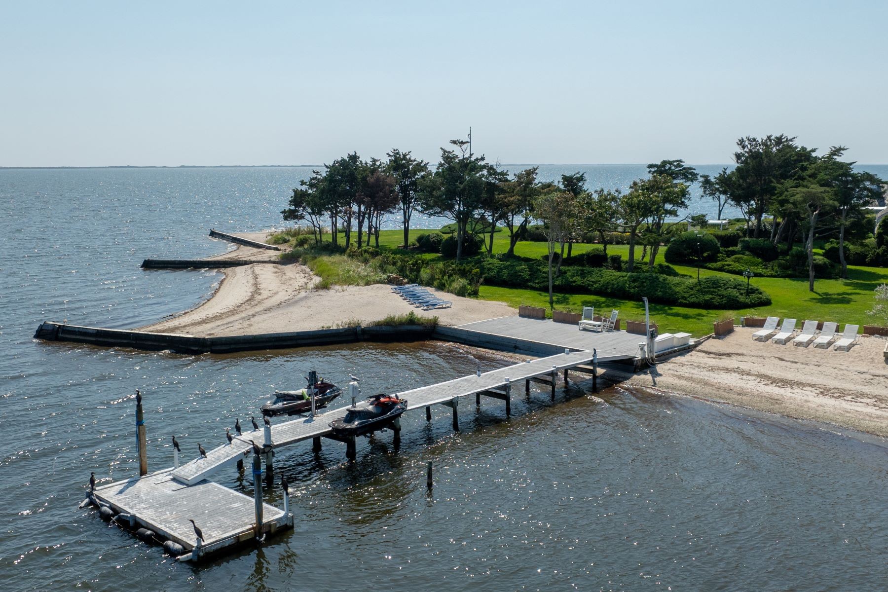 The deep-water dock at 16 Point Road reaching out over Great South Bay, two personal watercraft tied alongside, a sandy beach and lawn on the right