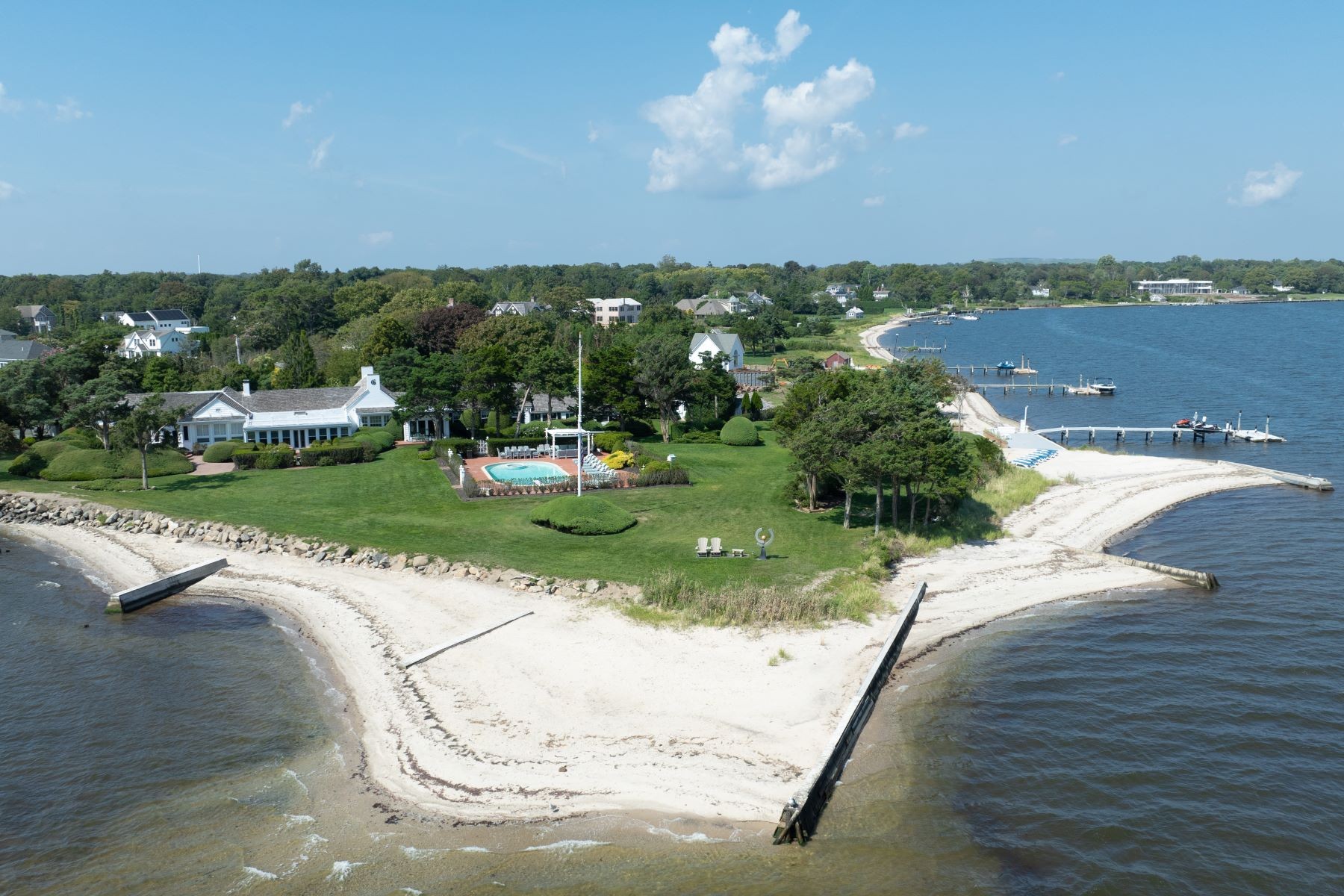 Aerial of the sandy point at 16 Point Road, a curved spit of beach reaching into Great South Bay with the dock and lawn behind it